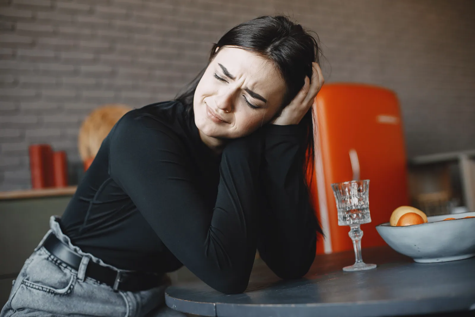 Una joven sentada a una mesa, con las manos en la cabeza y los ojos cerrados