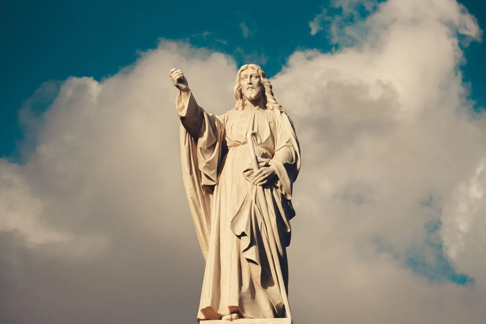 Estatua de Jesús con un brazo levantado, recortada contra un cielo con nubes
