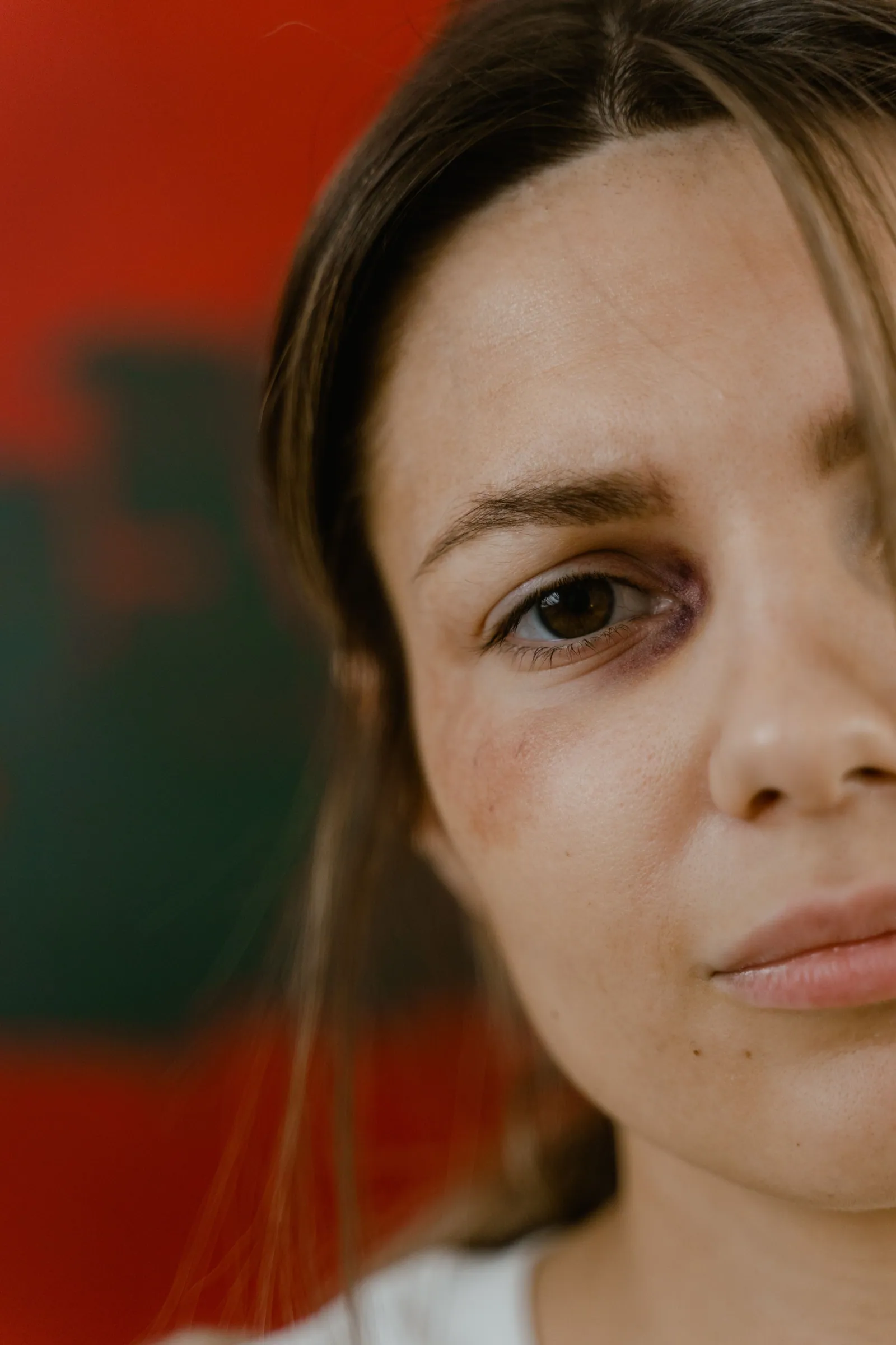 Primer plano del rostro de una joven, con la mitad de la cara en sombra y la mirada seria, fondo rojo desenfocado